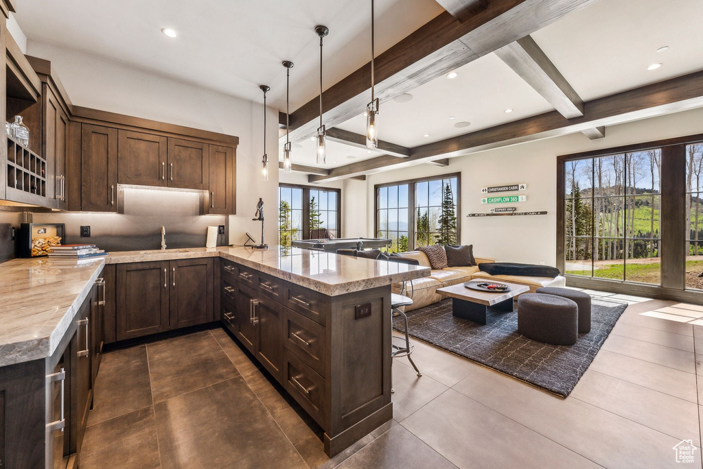 Kitchen featuring open floor plan, beamed ceiling, a peninsula, dark brown cabinets, and a sink