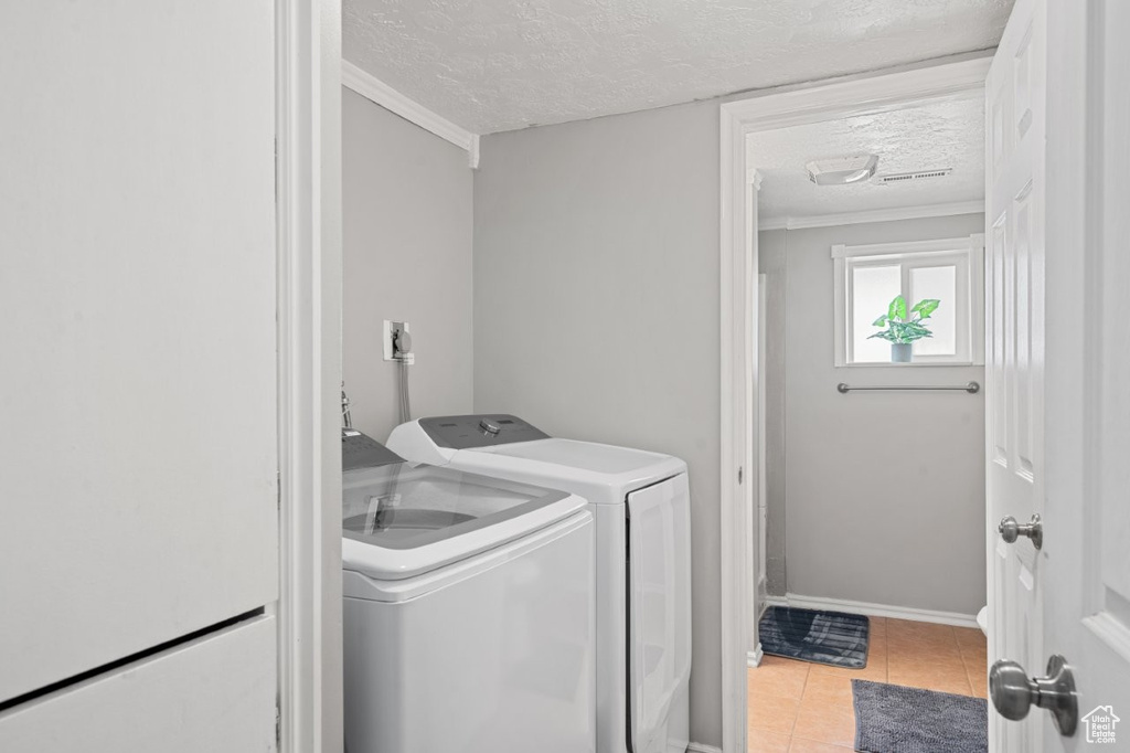 Washroom with washer and clothes dryer, a textured ceiling, light tile patterned floors, and ornamental molding