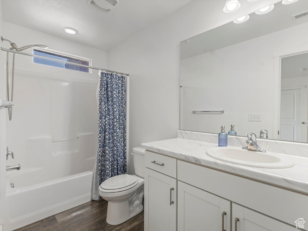 Full bath with toilet, wood finished floors, vanity, and shower / tub combo with curtain