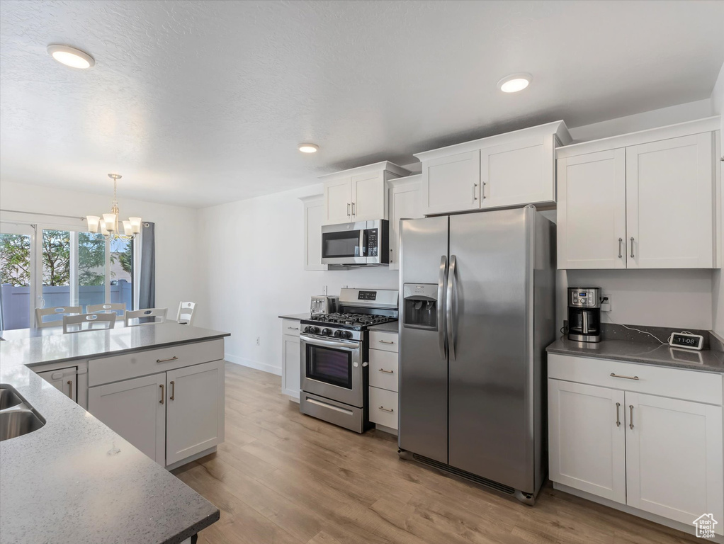 Kitchen with appliances with stainless steel finishes, a chandelier, light wood-style floors, white cabinets, and hanging light fixtures