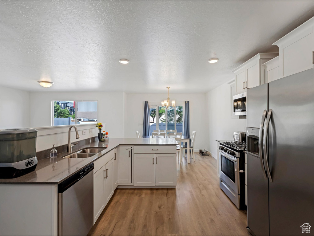 Kitchen with appliances with stainless steel finishes, a sink, light wood finished floors, a chandelier, and healthy amount of natural light