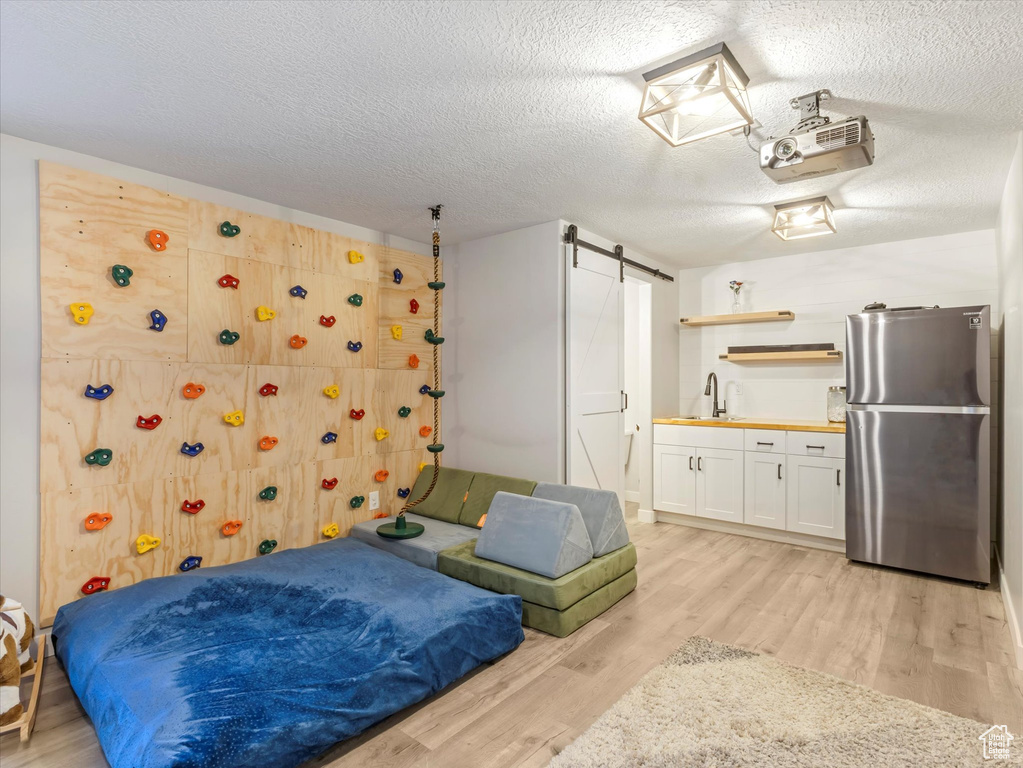 Bedroom with freestanding refrigerator, light wood-style floors, a textured ceiling, a barn door, and bar with sink