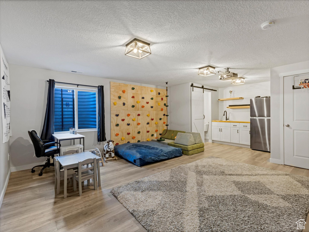 Bedroom featuring freestanding refrigerator, a barn door, light wood-type flooring, a textured ceiling, and baseboards