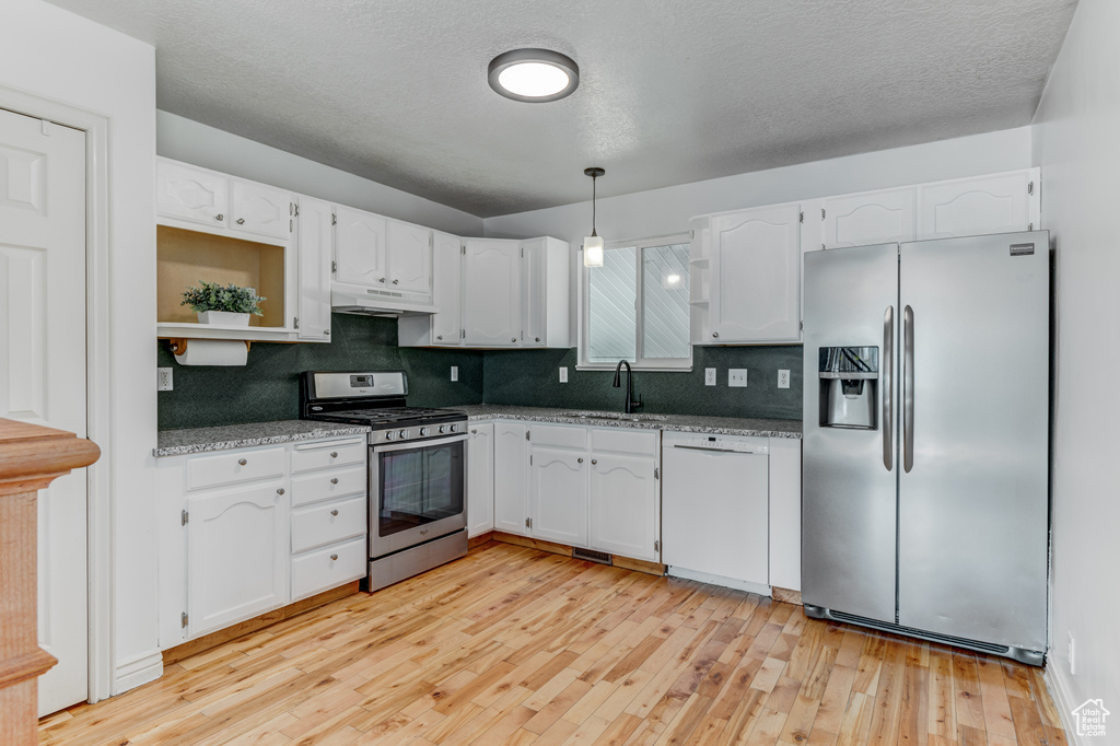 Kitchen featuring appliances with stainless steel finishes, white cabinets, under cabinet range hood, decorative backsplash, and light wood-style flooring