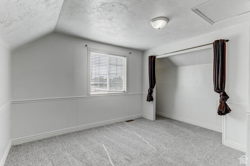 Unfurnished bedroom with a textured ceiling, carpet floors, vaulted ceiling, wainscoting, and attic access