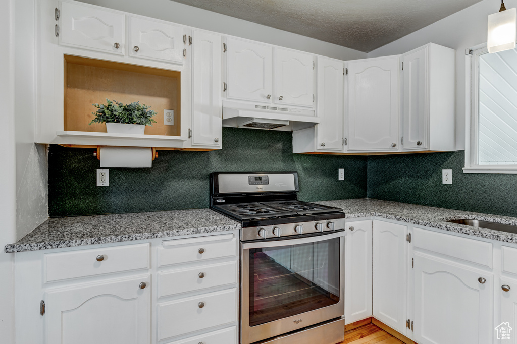 Kitchen with gas stove, under cabinet range hood, white cabinets, tasteful backsplash, and a textured ceiling