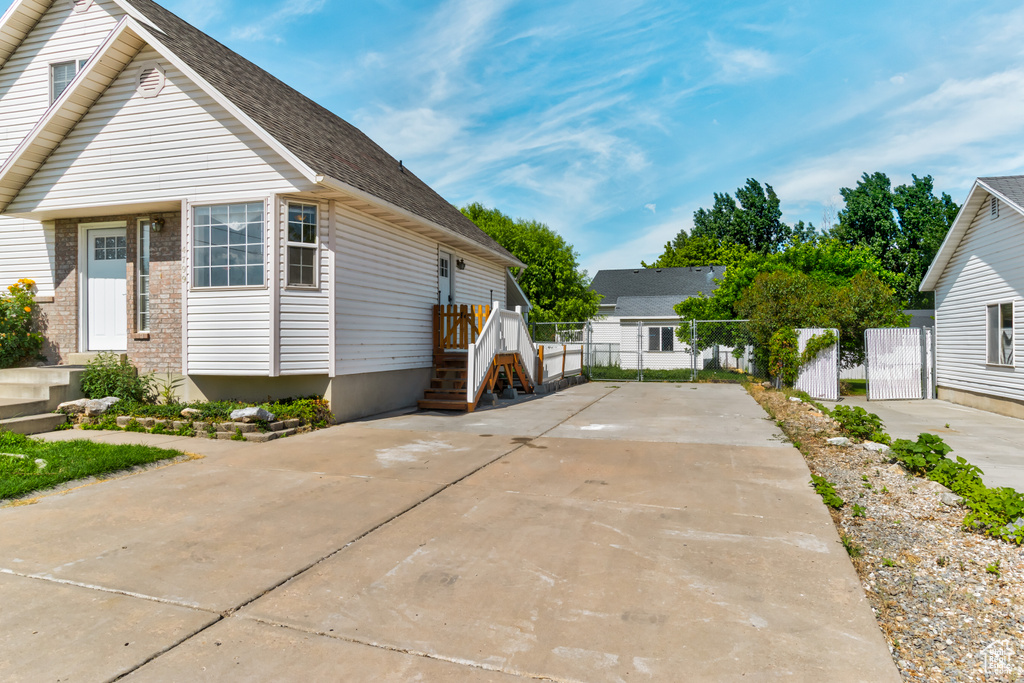 View of front facade with driveway, a gate, and roof with shingles