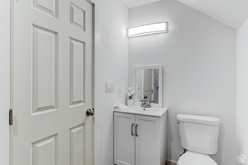 Half bath with vanity, toilet, and lofted ceiling