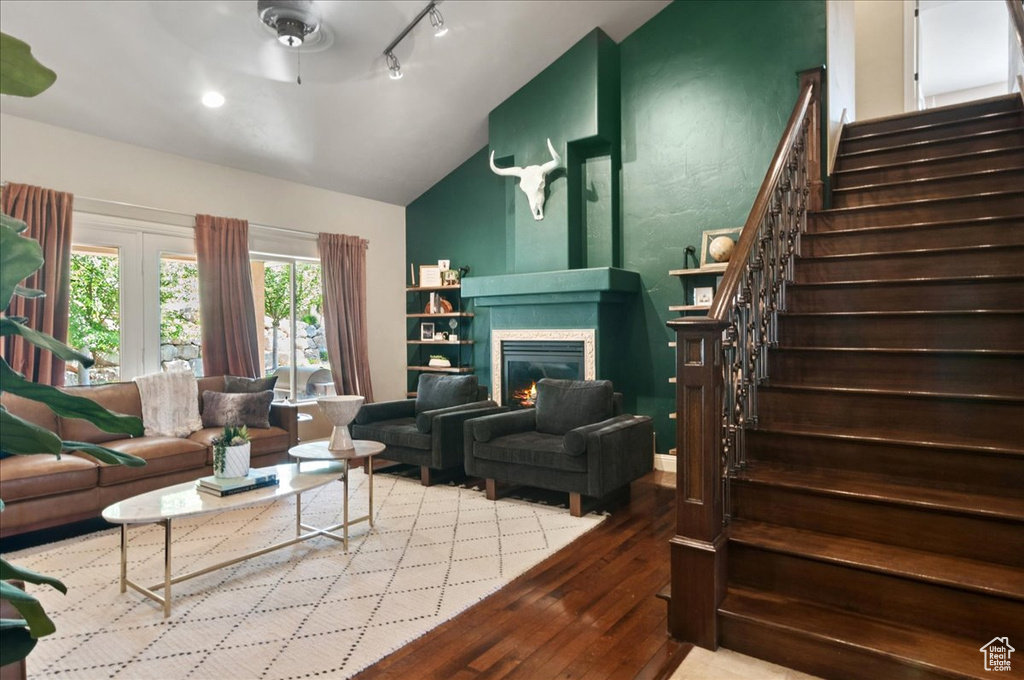 Living area with lofted ceiling, stairway, wood-type flooring, a glass covered fireplace, and ceiling fan