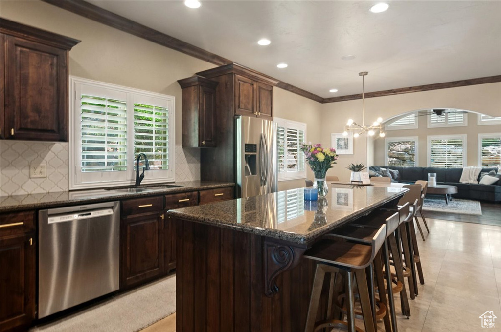 Kitchen featuring appliances with stainless steel finishes, a sink, crown molding, open floor plan, and dark stone counters