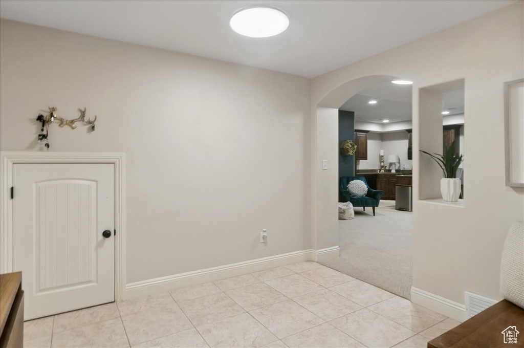 Empty room featuring arched walkways, light tile patterned flooring, baseboards, and light colored carpet
