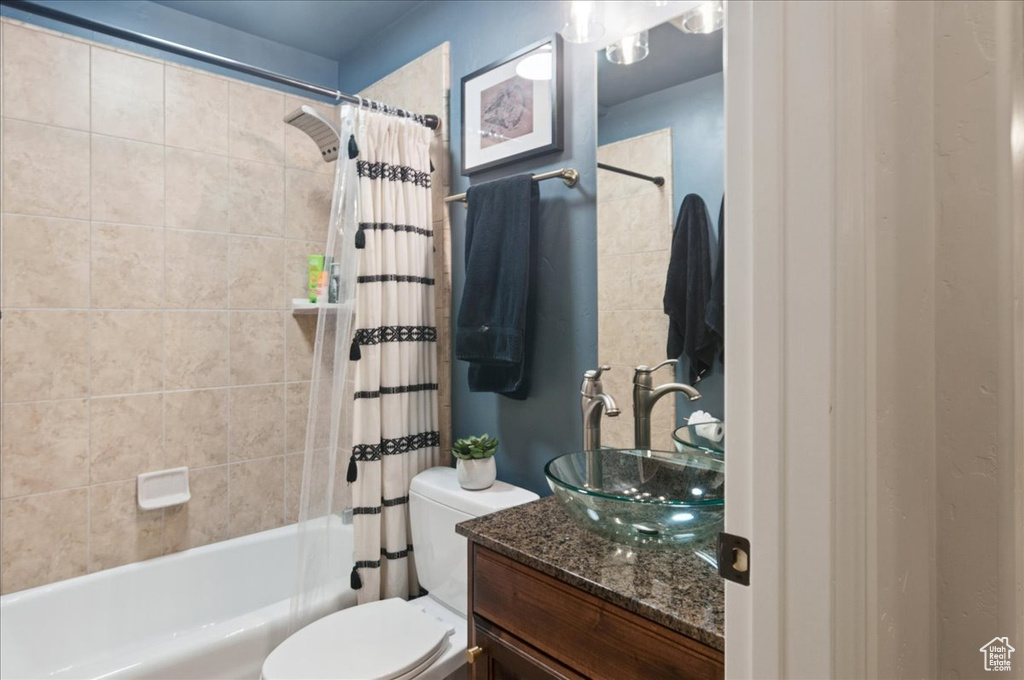 Bathroom featuring vanity, shower / tub combo with curtain, and toilet