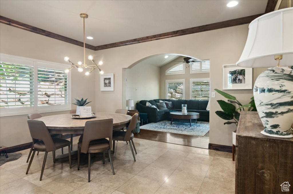 Dining room with crown molding, arched walkways, a chandelier, baseboards, and ceiling fan