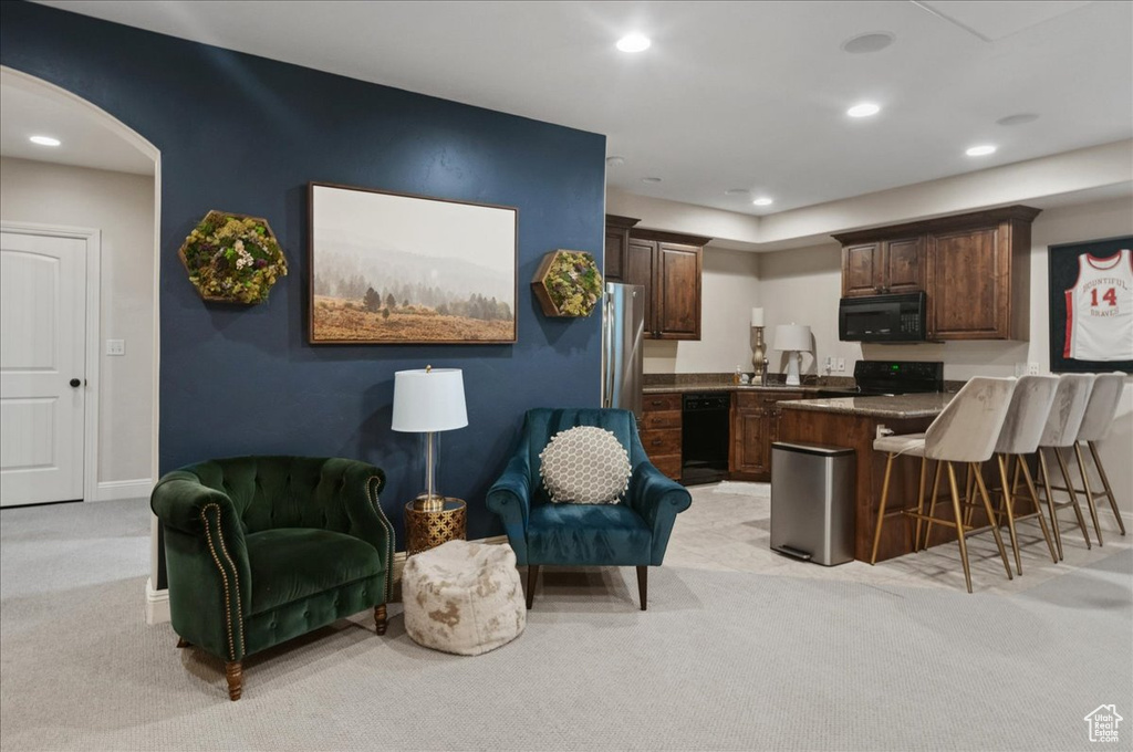 Kitchen featuring black appliances, light colored carpet, a breakfast bar area, a peninsula, and dark countertops