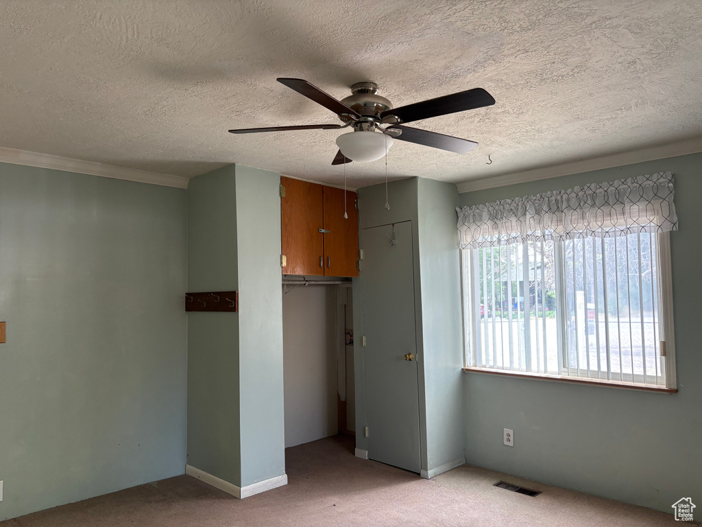 Unfurnished bedroom with a closet, light colored carpet, a textured ceiling, a ceiling fan, and crown molding