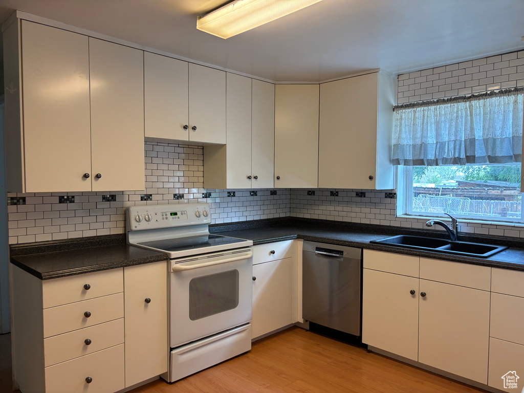 Kitchen featuring white range with electric cooktop, dishwasher, a sink, light wood-style flooring, and dark countertops