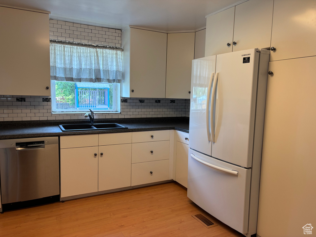 Kitchen with freestanding refrigerator, stainless steel dishwasher, a sink, dark countertops, and light wood-type flooring
