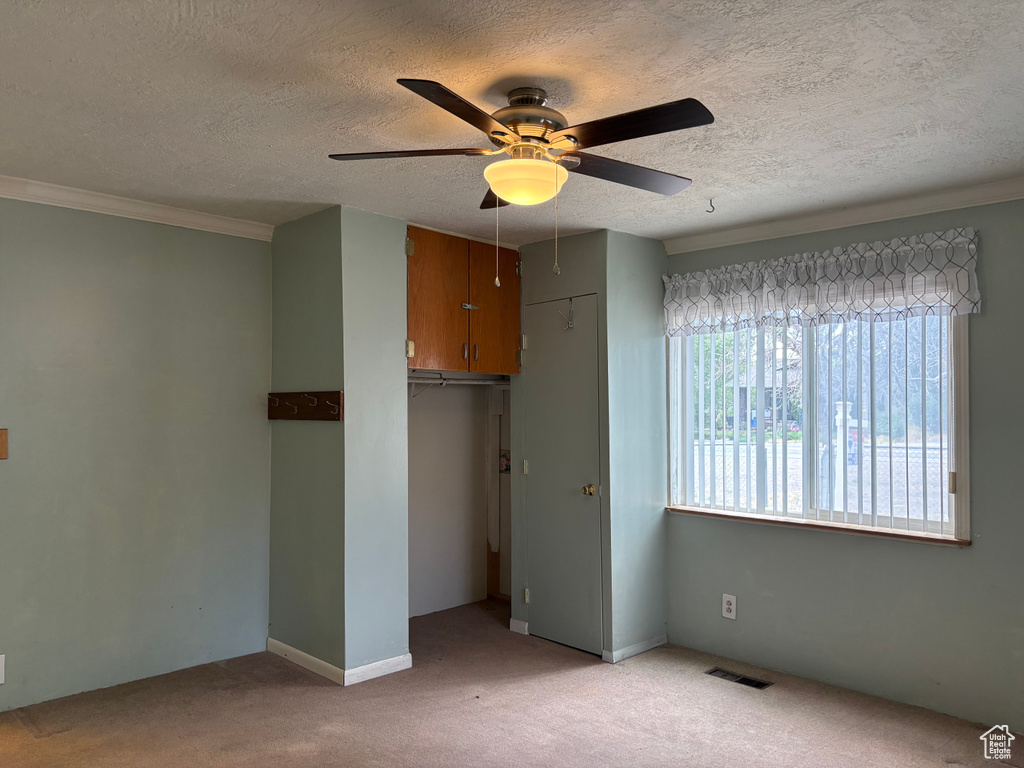 Unfurnished bedroom with a closet, a textured ceiling, light carpet, crown molding, and ceiling fan