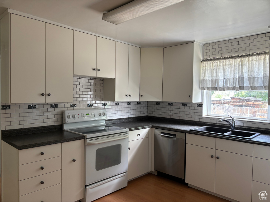 Kitchen featuring white electric range, stainless steel dishwasher, dark countertops, and a sink