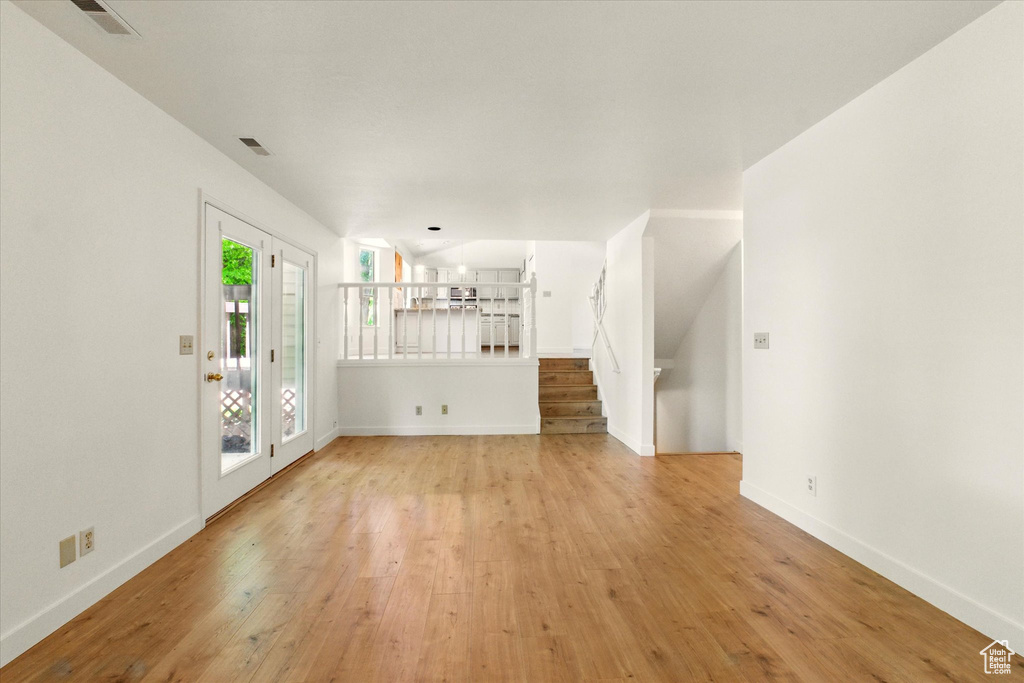 Unfurnished living room featuring light wood-style flooring, baseboards, and stairs