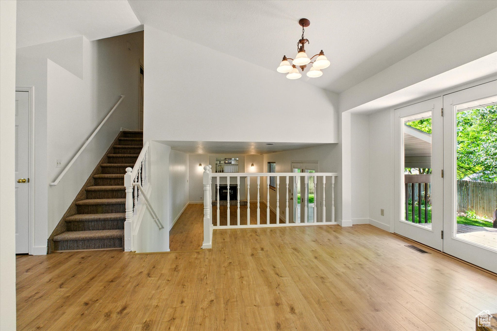 Unfurnished living room featuring a chandelier, wood finished floors, high vaulted ceiling, baseboards, and stairway