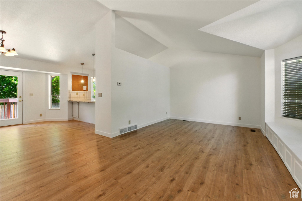 Unfurnished living room featuring lofted ceiling, light wood-type flooring, and baseboards