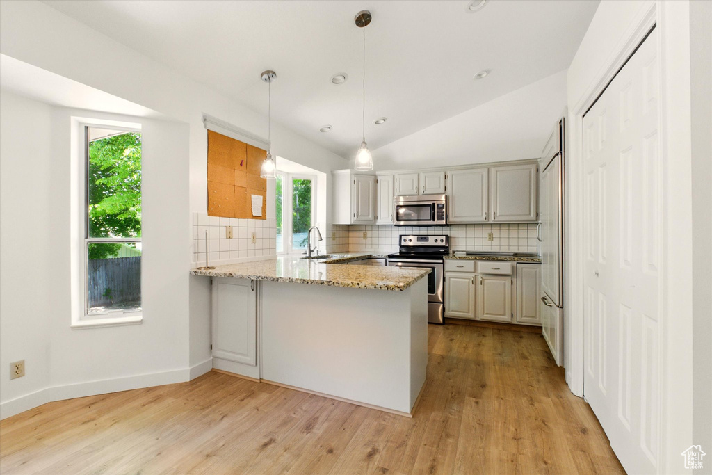 Kitchen featuring appliances with stainless steel finishes, a peninsula, backsplash, plenty of natural light, and vaulted ceiling