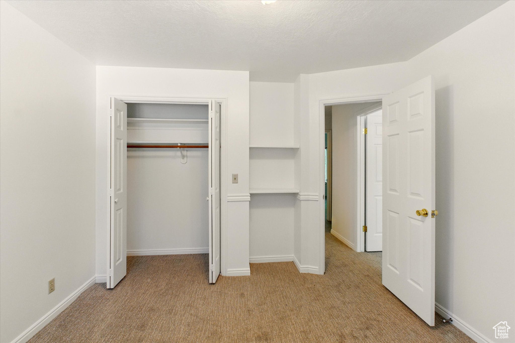 Unfurnished bedroom with light carpet, a closet, and baseboards