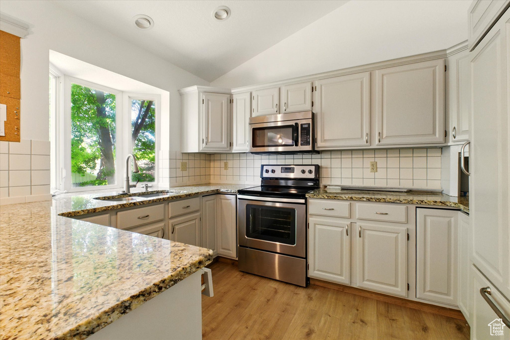 Kitchen featuring appliances with stainless steel finishes, a sink, lofted ceiling, light wood-type flooring, and light stone countertops