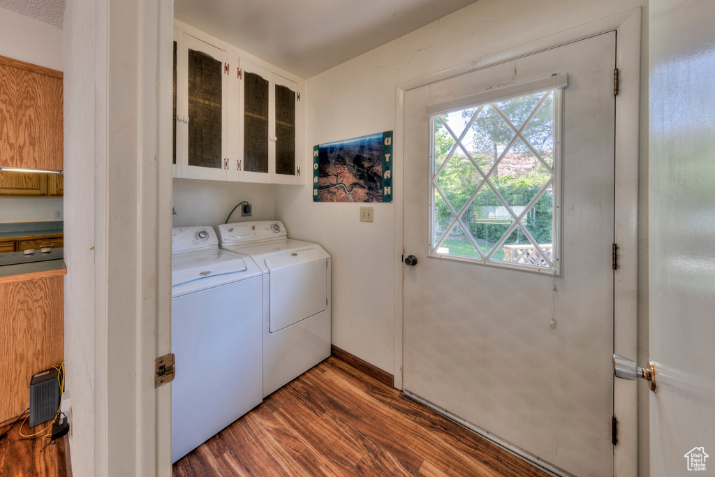 Washroom featuring cabinet space, washing machine and dryer, healthy amount of natural light, and wood finished floors
