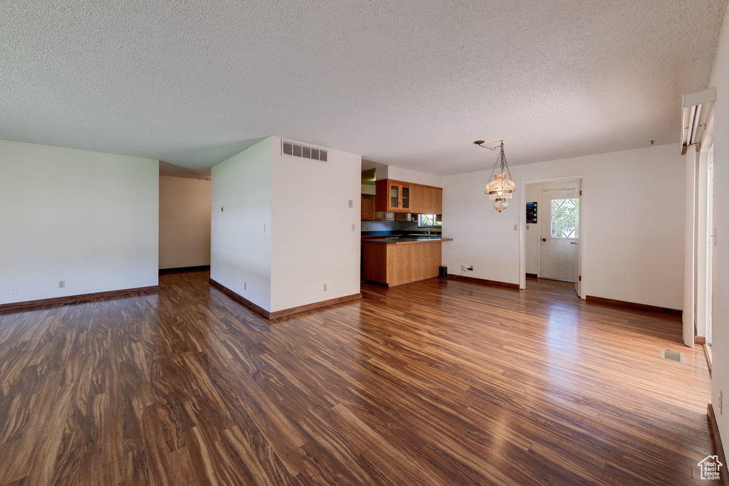 Unfurnished living room featuring a textured ceiling, dark wood-type flooring, a chandelier, and baseboards