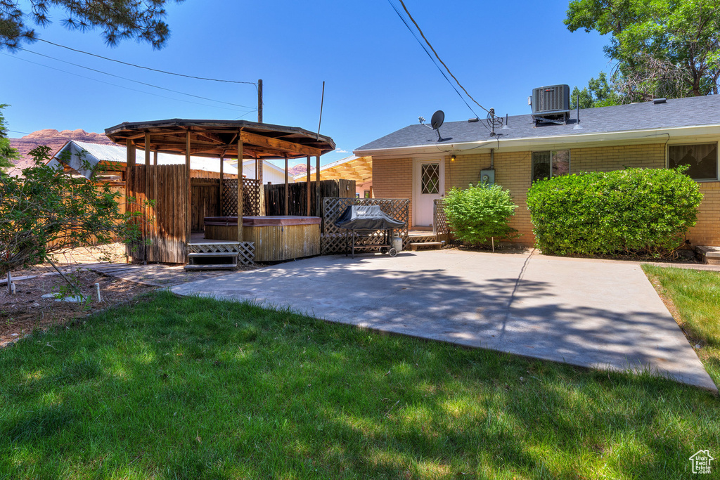 Rear view of property featuring a hot tub, brick siding, a patio area, and roof with shingles