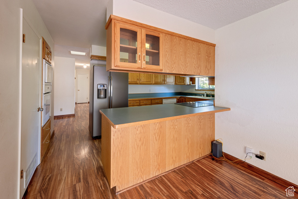 Kitchen with stainless steel fridge with ice dispenser, dark wood finished floors, a peninsula, glass insert cabinets, and black electric stovetop