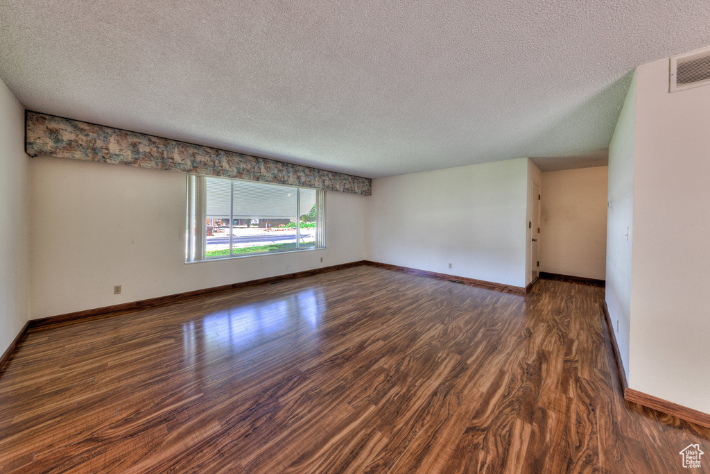 Empty room with a textured ceiling, wood finished floors, and baseboards