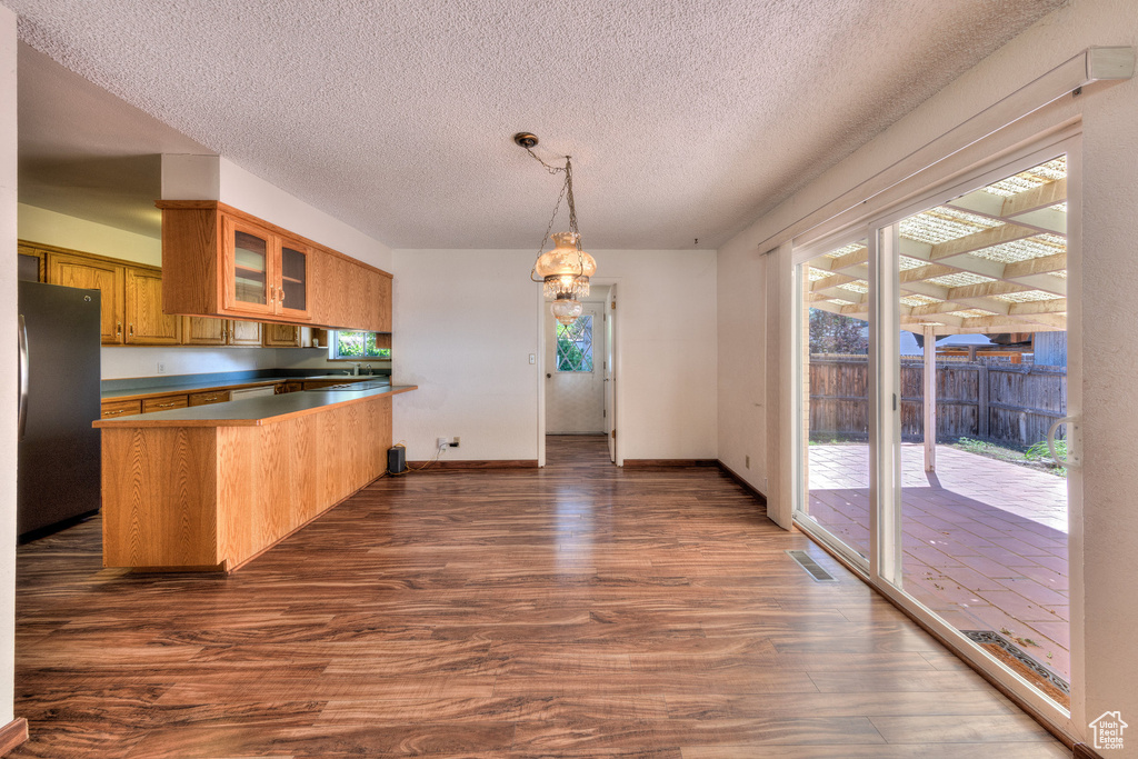 Kitchen with freestanding refrigerator, a peninsula, dark wood-style floors, brown cabinets, and glass insert cabinets