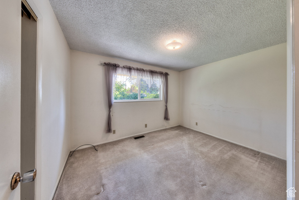 Carpeted spare room featuring a textured ceiling and baseboards