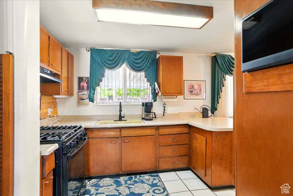 Kitchen with black range with gas cooktop, a sink, and brown cabinets