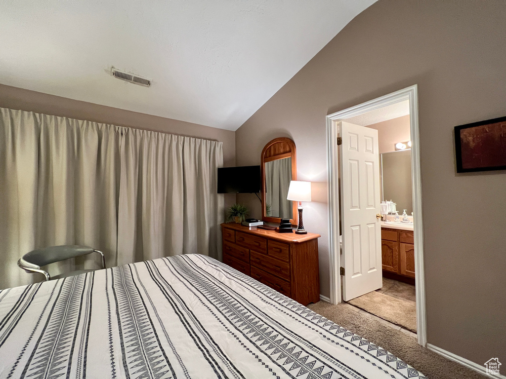 Bedroom with lofted ceiling, light carpet, baseboards, and ensuite bath