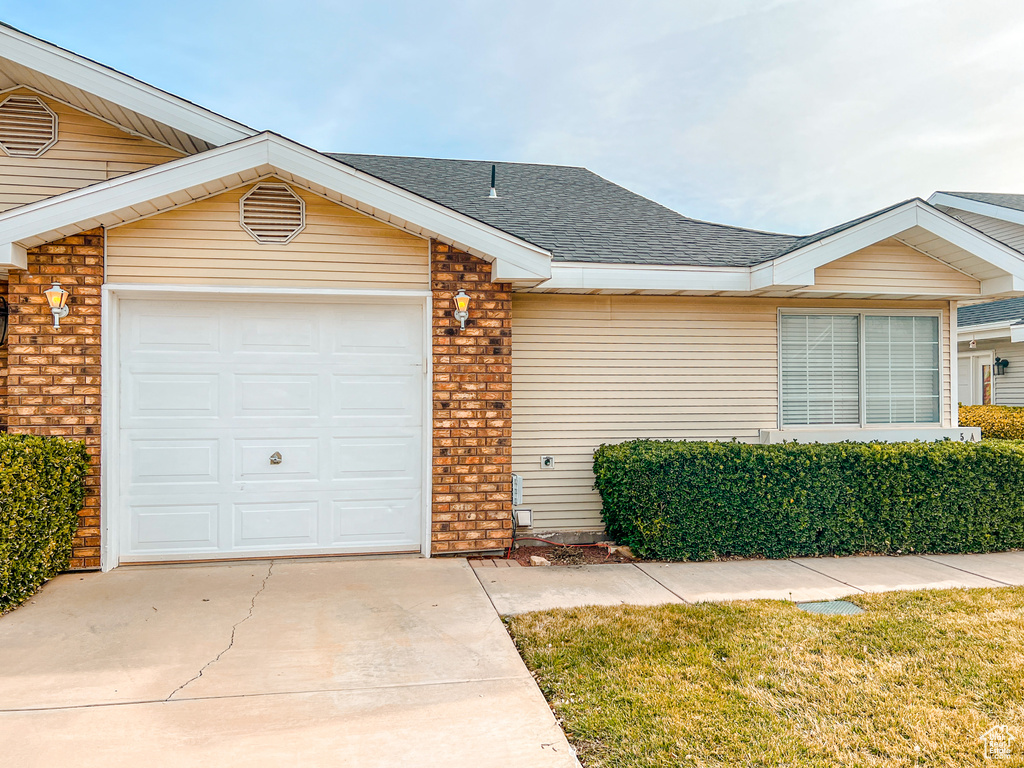 Single story home with driveway, roof with shingles, a garage, and brick siding