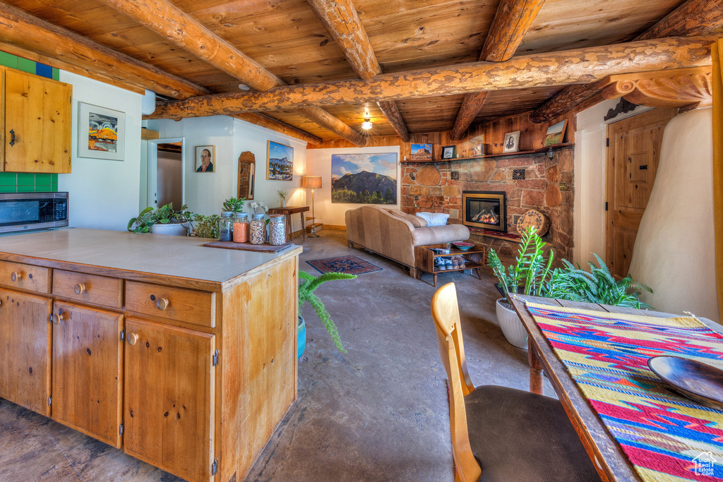 Kitchen with a fireplace, wood ceiling with exposed beams, stainless steel microwave, concrete floors, and light countertops