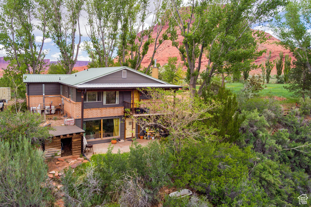 Back of property with a patio area, brick siding, a chimney, and metal roof