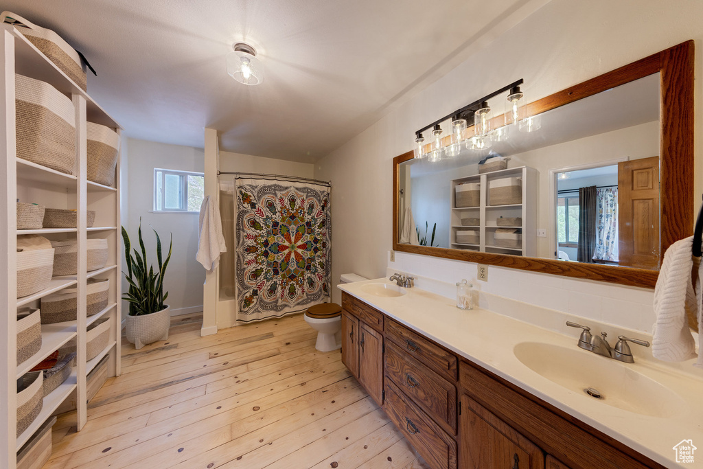 Full bath with toilet, double vanity, a shower with curtain, and wood-type flooring
