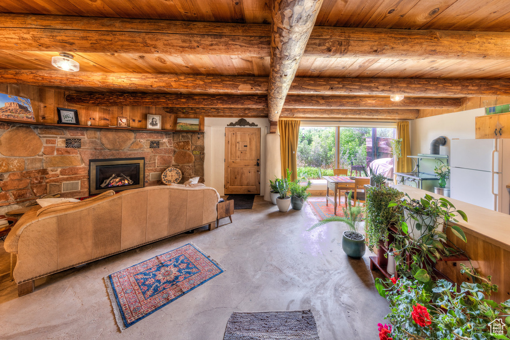 Living room featuring wooden ceiling with exposed beams, concrete floors, and a stone fireplace