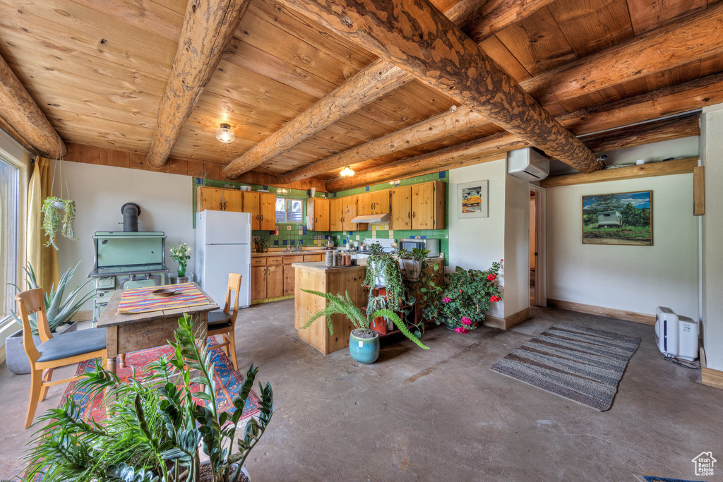 Kitchen featuring freestanding refrigerator, wooden ceiling with exposed beams, unfinished concrete flooring, under cabinet range hood, and a wood stove