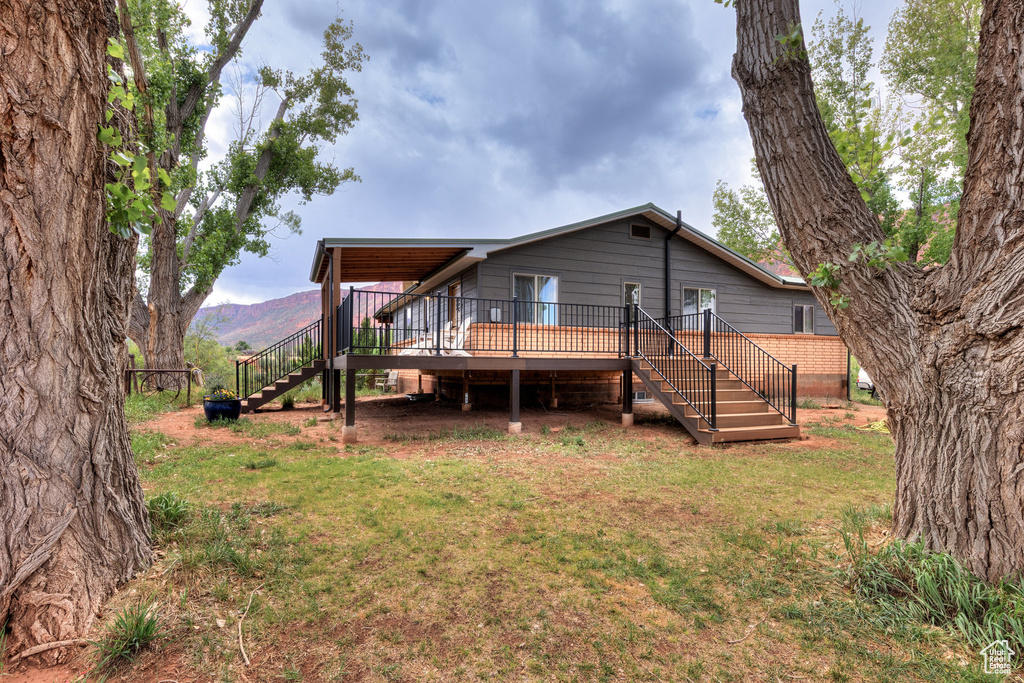 Rear view of house featuring stairs, a deck with mountain view, and a lawn