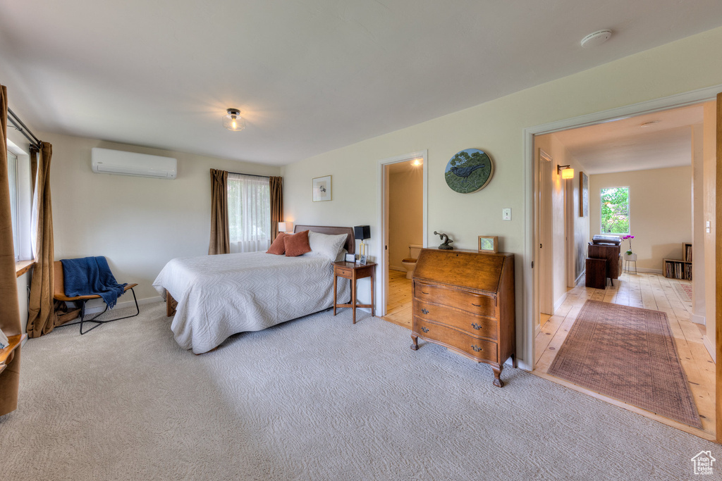 Bedroom featuring a wall mounted air conditioner, light carpet, and baseboards