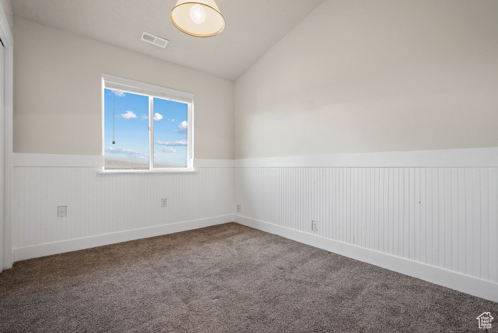 Empty room featuring wainscoting, carpet flooring, and vaulted ceiling