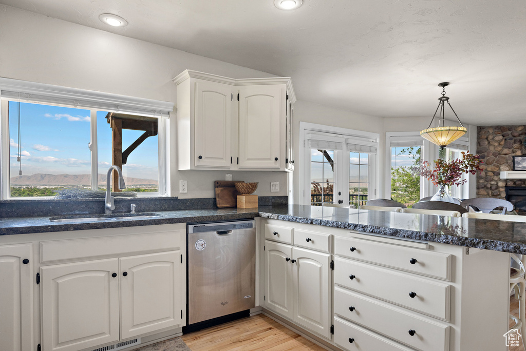Kitchen featuring stainless steel dishwasher, a sink, a peninsula, white cabinetry, and healthy amount of natural light