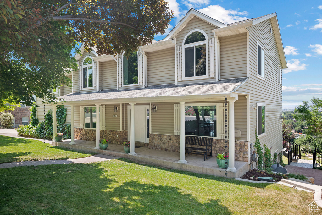 View of front of home featuring a porch, a front lawn, stone siding, and roof with shingles