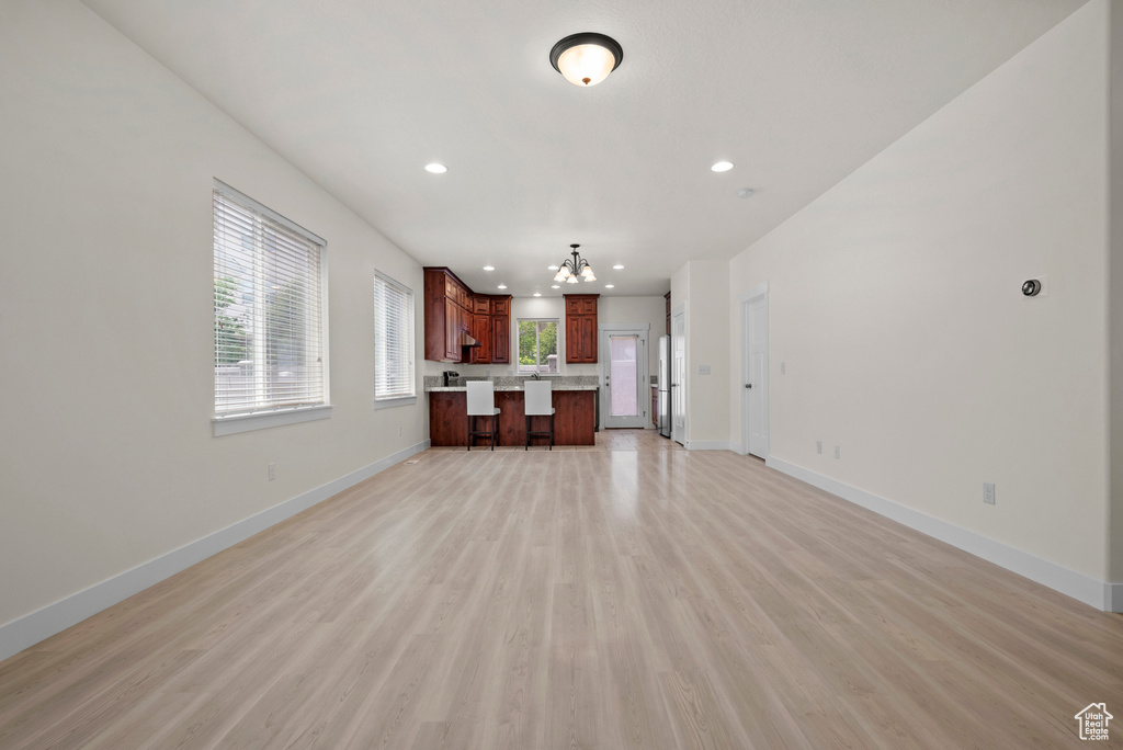 Unfurnished living room with a chandelier, light wood-style flooring, baseboards, and recessed lighting